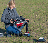 Woman in a field using the mobile IMAGING-PAM system to probe cereals in the tillering stage